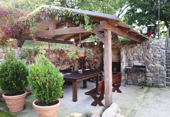 Terrasse couverte en pierre avec table et bancs en bois, plantes en pot et barbecue à Miedzyzdroje, Allemagne.