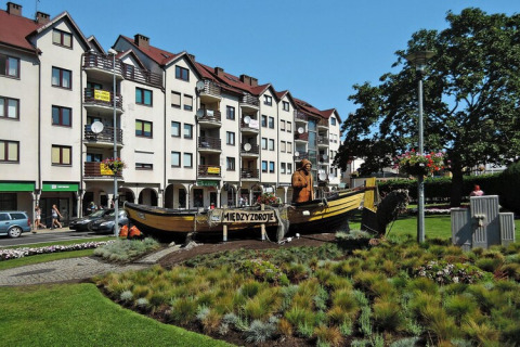Rotonde met vissersboot en beeld in Międzyzdroje, voor moderne appartementen op een zonnige dag.
