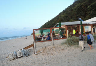 Strandrestaurant mit Gästen und Spaziergängern am Sand bei Ferienhäusern in Miedzyzdroje nahe dem Meer.