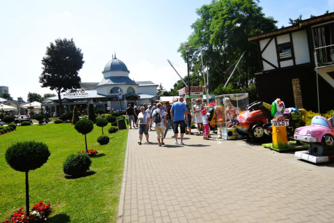 Outdoor view of holiday homes in Miedzyzdroje with people walking, playground rides, and a restaurant in the back.