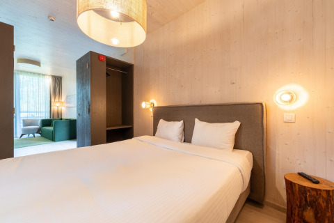 Alojamiento glamping moderno con cama doble, armario abierto y zona de estar con sofá verde.