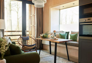 Cozy tiny house living area with green sofa, dining table and large window at The Lodge by YourNature.
