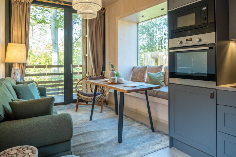 Gemütliche Glamping-Unterkunft mit modernem Küchenbereich, Esstisch und großen Fenstern zur Natur.