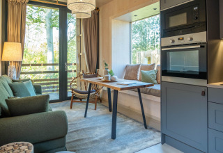 Cozy glamping accommodation featuring a modern kitchen, dining table, and large windows with forest views.