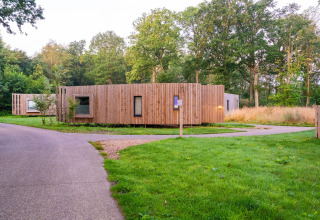 Moderne tiny house med træfacade i grønne omgivelser og natur, omgivet af stier og træer.