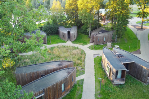 Luftaufnahme von modernen Glamping-Hütten aus Holz, malerisch zwischen Bäumen im Grünen verteilt.