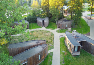 Aerial view of unique wooden glamping cabins arranged in a circle among lush greenery and trees.