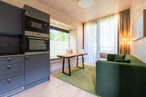 Moderne glampingbolig med grøn sofa, spisebord, stort vindue og køkken med indbygget ovn og mikroovn.