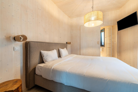 Moderne glamping-indkvartering med dobbeltseng, trævægge, natbord og vægmonteret tv i soveværelset.