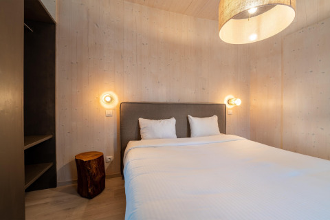 Gemütliches Glamping-Schlafzimmer mit Doppelbett, Baumstumpf-Tisch, Holzverkleidung und Wandlampen.