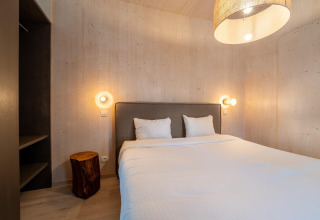 Moderne glamping-soveværelse med dobbeltseng, træstub-bord, træpaneler og bløde væglamper.