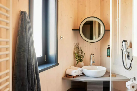 Moderne badeværelse med trævægge, rundt spejl, håndvask og håndklæder i The Lodge af YourNature.