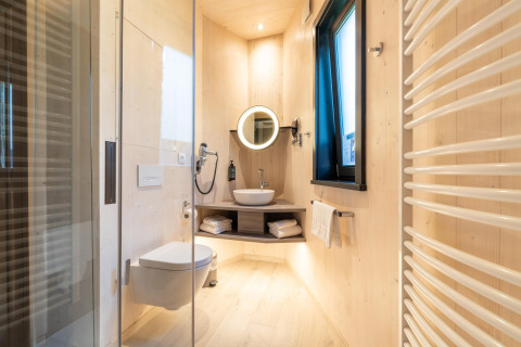 Modern bathroom in a glamping accommodation with wood paneling, shower, mounted toilet, and large window.