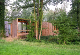 Et lille træhus ved navn The Lodge af YourNature, gemt væk i en grøn, skovklædt natur omgivet af træer.