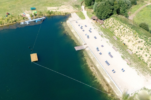 Luchtfoto van een glampinglocatie met zandstrand, ligstoelen en kajaks bij een rustige oever van het meer.