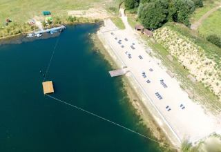 Luchtfoto van een glampinglocatie met zandstrand, ligstoelen en kajaks bij een rustige oever van het meer.