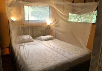 Slaapkamer in een safaritent met twee eenpersoonsbedden, klamboe en ramen met uitzicht op de natuur.