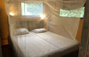 Camera da letto in tenda safari con due letti singoli, zanzariera e finestre con vista sulla natura.