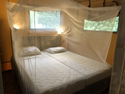 Een slaapkamer in een safaritent met twee enkele bedden, muskietennet en ramen met natuurzicht.