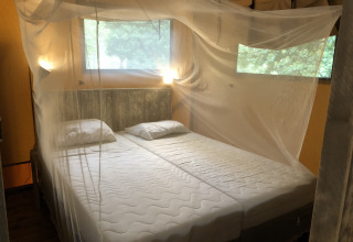 Een slaapkamer in een safaritent met twee enkele bedden, muskietennet en ramen met natuurzicht.