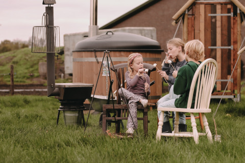 Trois enfants grillent des guimauves au feu devant une cabane à Feather Down De Oude Melkstal, Pays-Bas.