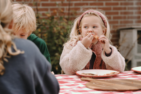 Bambini che mangiano pizza all’aperto su un tavolo a quadri al Feather Down De Oude Melkstal, Brabante Settentrionale.