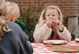 Kinderen eten buiten pizza aan een geblokte tafel in Feather Down De Oude Melkstal, Noord-Brabant, Nederland.