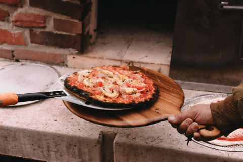 Eine frisch gebackene Pizza wird aus einem Holzofen im Feather Down De Oude Melkstal Ferienpark geholt.