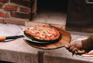 Freshly baked pizza being taken out of a wood-fired oven at Feather Down De Oude Melkstal holiday park, Netherlands.