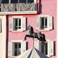 Caballo negro de carrusel frente a edificios coloridos con contraventanas en Méolans-Revel, Provence-Alpes-Côte d’Azur.