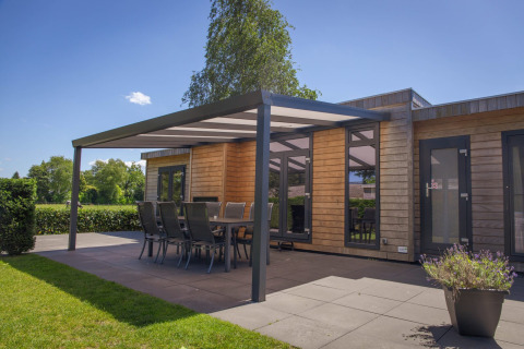 Modern glampingverblijf met houten buitenkant, overdekt terras, eettafel en stoelen in het groen.