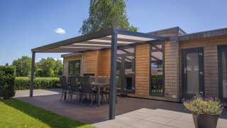 Cabaña glamping moderna de madera con terraza cubierta, mesa comedor y sillas, rodeada de naturaleza.