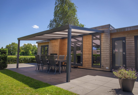 Cabaña glamping moderna de madera con terraza cubierta, mesa comedor y sillas, rodeada de naturaleza.