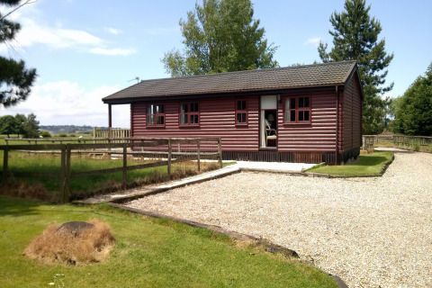 Et foto af Five Waterings, en hyggelig træchalet med indhegnet have og grussti i landlige omgivelser.