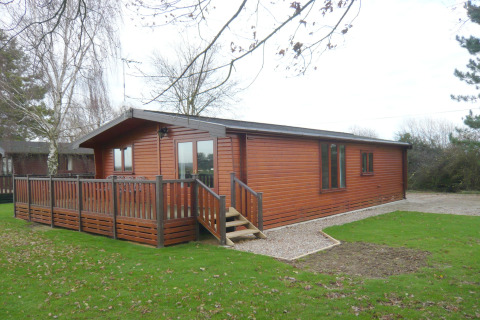 Foto del lodge Rainbow Petty con esterno in legno, veranda, prato verde e alberi tutt’intorno.