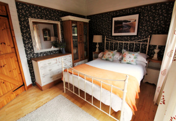 Camera da letto nel chalet Five Waterings, Regno Unito, con letto matrimoniale, specchio e carta da parati floreale.