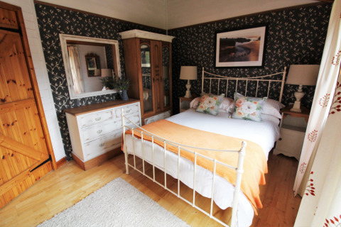 Soveværelse i Five Waterings chalet, Storbritannien, med dobbeltseng, spejl og blomstret tapet.