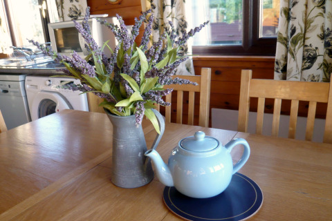 Træbord med lyseblå tekande, kunstige lavendelblomster i kande, i chalet Five Waterings, Storbritannien.