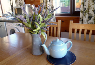 Træbord med lyseblå tekande, kunstige lavendelblomster i kande, i chalet Five Waterings, Storbritannien.