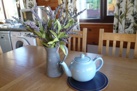 Træbord med lyseblå tekande, kunstige lavendelblomster i kande, i chalet Five Waterings, Storbritannien.