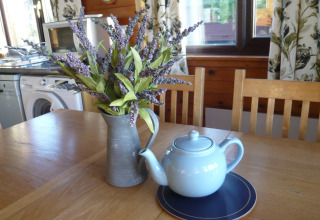 Træbord med lyseblå tekande, kunstige lavendelblomster i kande, i chalet Five Waterings, Storbritannien.