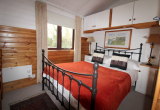 Soveværelse i chalet 'Five Waterings' i Storbritannien med jernseng, træpaneler og rød plaid.