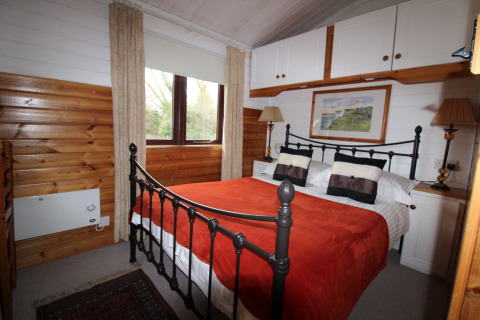 Soveværelse i chalet 'Five Waterings' i Storbritannien med jernseng, træpaneler og rød plaid.