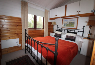 Soveværelse i chalet 'Five Waterings' i Storbritannien med jernseng, træpaneler og rød plaid.