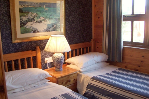 Et hyggeligt værelse på 'Five Waterings' chalet i Storbritannien med to enkeltsenge og en lampe.