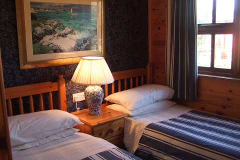 Et hyggeligt værelse på 'Five Waterings' chalet i Storbritannien med to enkeltsenge og en lampe.