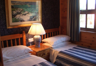 Et hyggeligt værelse på 'Five Waterings' chalet i Storbritannien med to enkeltsenge og en lampe.