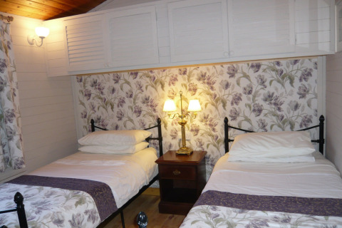 To enkeltsenge i et hyggeligt værelse med blomstrede tapeter i Five Waterings chalet, Storbritannien.
