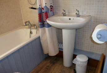 Bagno compatto presso il chalet Five Waterings con vasca, tenda nautica, lavabo e carta igienica.