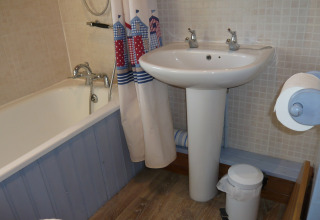 Et kompakt badeværelse på Five Waterings med badekar, forhæng, håndvask, toiletspand og toiletrulle.
